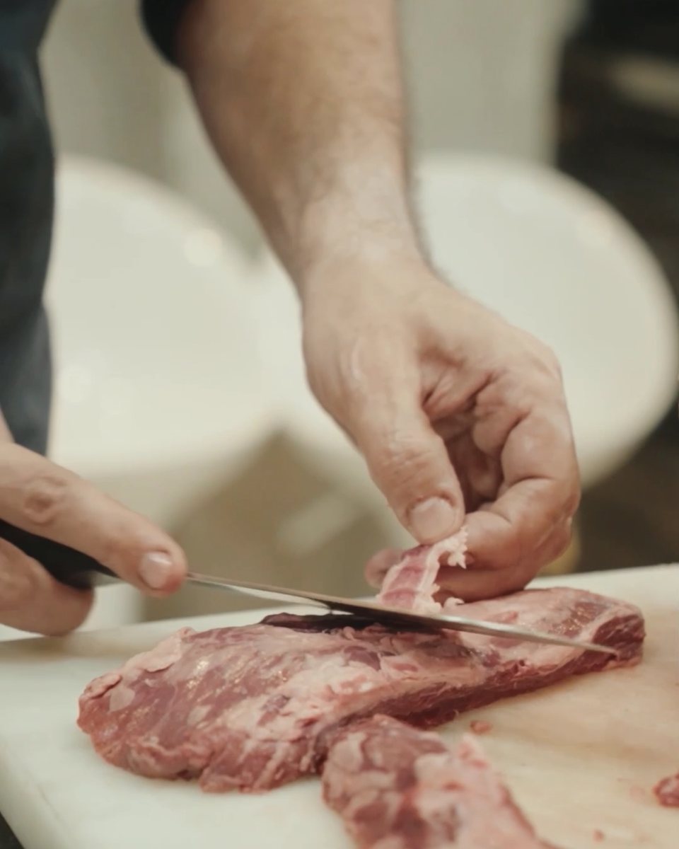 Chef Moreno Benigno's hands trimming a cut of beef in the kitchen