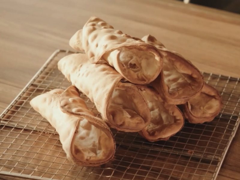 Freshly fried cannoli shells cooling on a rack